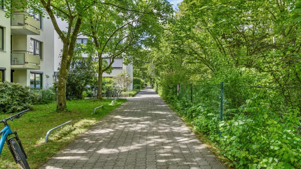Begrünter Zugangsweg zur Wohnanlage in München-Forstenried mit Fahrradabstellplatz und dichtem Grün