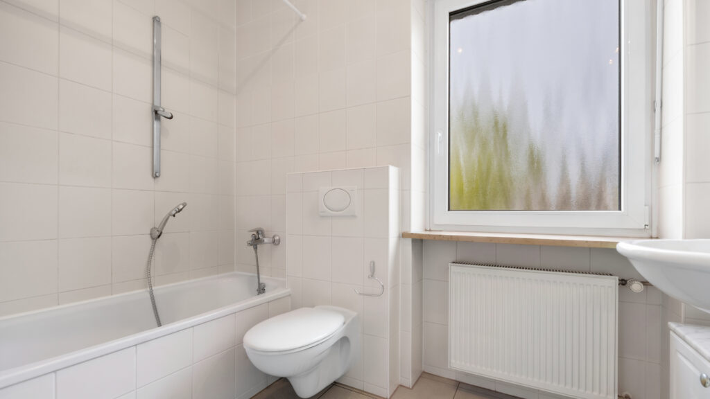 Existing bathroom with white tiles, bathtub, and toilet in the house for purchase in Munich-Obermenzing
