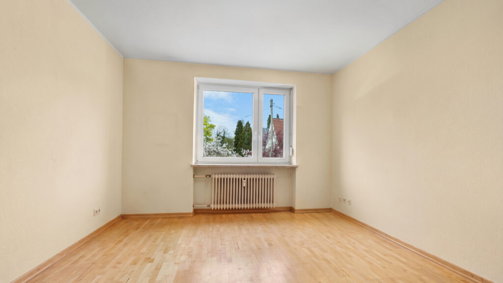 Empty room with beige walls, parquet flooring, and a view of a church steeple on the upper floor of the house in Obermenzing