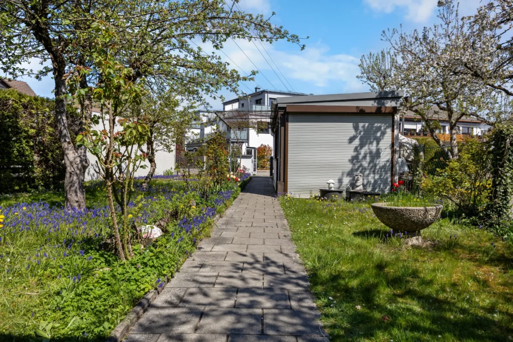 Paved garden path with blooming trees leading to the garage in Munich-Untermenzing – Rogers Immobilien