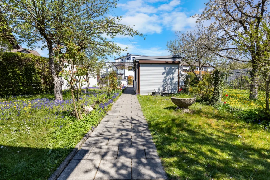 Paved garden path between blooming trees leading to the garage in Munich-Untermenzing – Rogers Immobilien