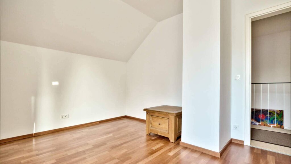Empty attic room with sloping ceiling and small dresser in Munich-Obermenzing – Rogers Immobilien