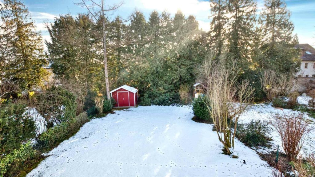 Snowy garden with a red garden shed and trees in Munich-Obermenzing – Rogers Immobilien