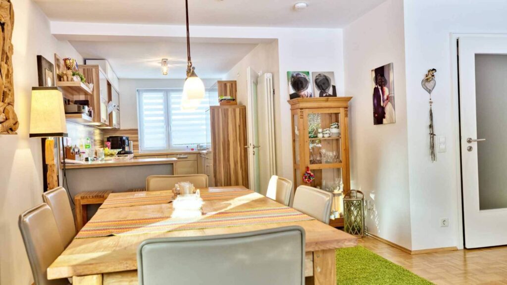 Dining area with wooden table and display cabinet open to the kitchen in a house in Munich-Obermenzing – Rogers Immobilien